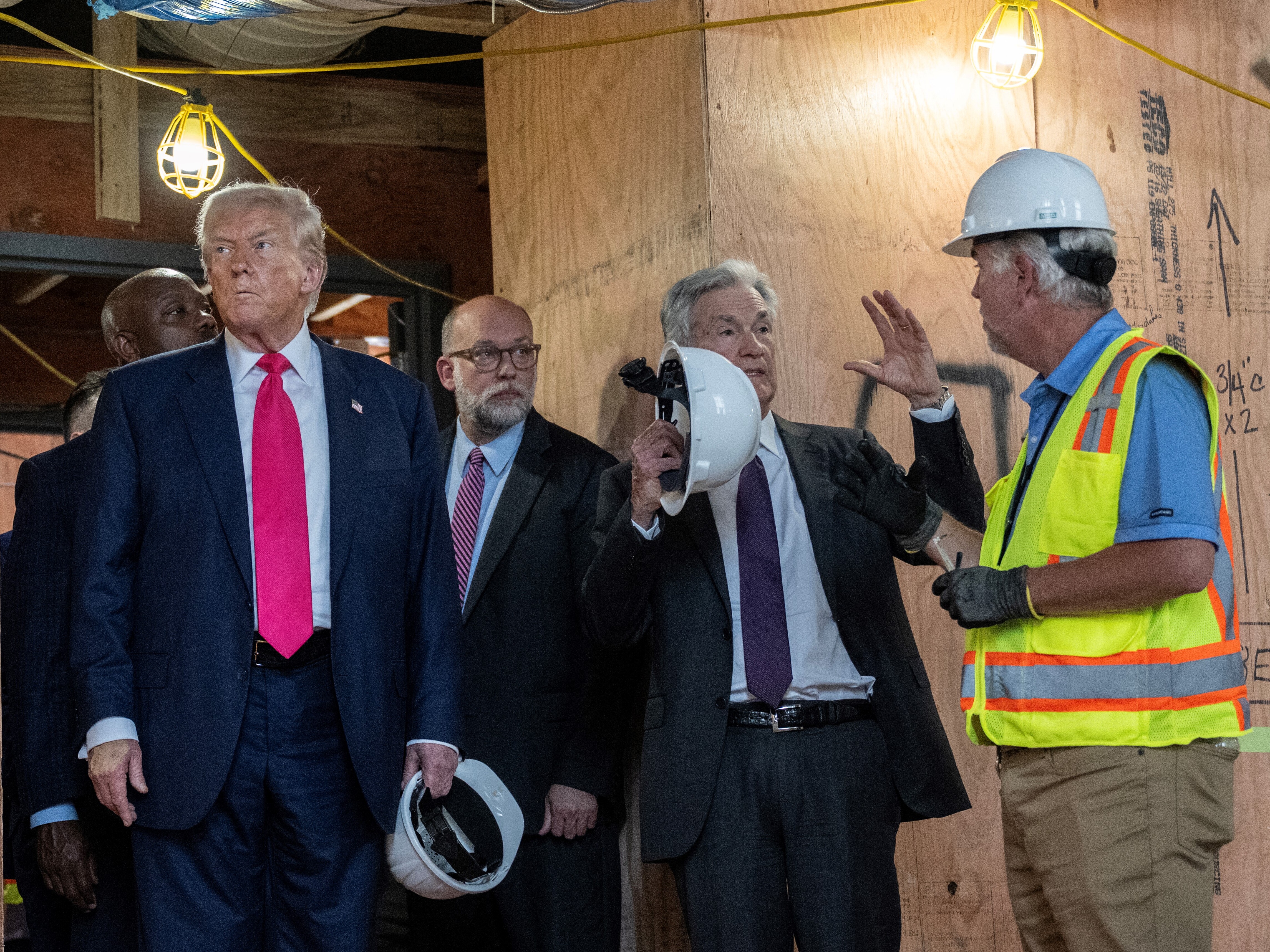caption: Federal Reserve Chair Jerome Powell (holding up hard hat) speaks with the construction manager during a tour of renovations at the Federal Reserve in Washington, D.C., on Thursday. At left is President Trump, and between Trump and Powell is the director of the Office of Management and Budget, Russell Vought.