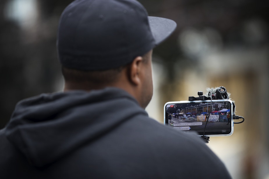 caption: Omari Salisbury, a journalist with Converge Media, live-streams at the intersection of 12th and Pine Streets on Monday, June 29, 2020, inside the Capitol Hill Organized Protest zone in Seattle. Earlier that morning, a 16-year-old boy was killed and a 14-year-old boy was critically injured in a shooting.