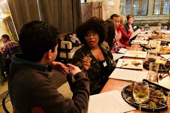 caption: Ishea Brown talks with Joe Santiago at KUOW's first Pop-Up Curiosity Club dinner at The Cloud Room in Seattle. February 28, 2019. 