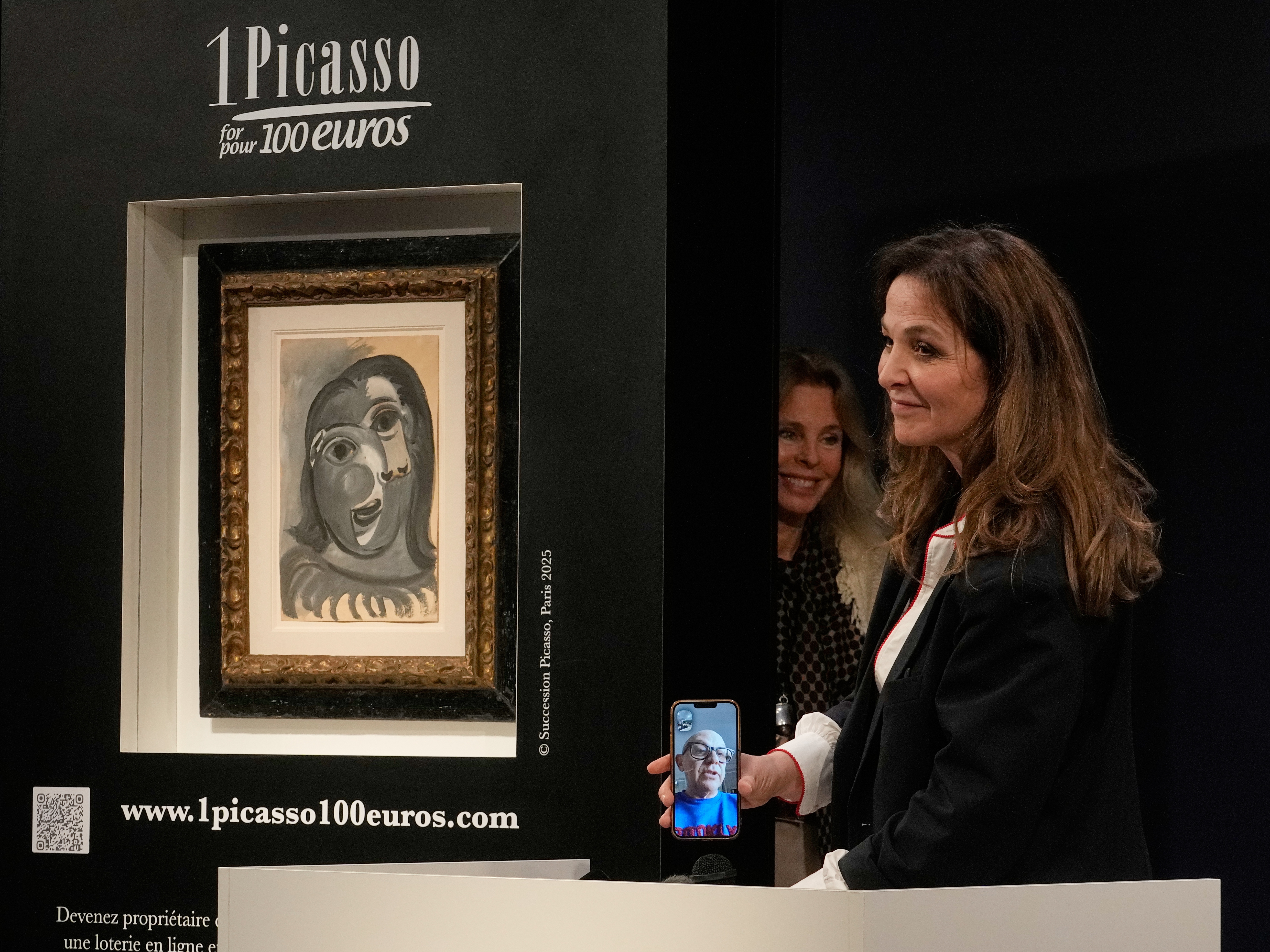 caption: Peri Cochin, right, founder of "1 Picasso for 100 euros," speaks on the phone with the winner, Ari Hodara of Paris, next to the painting 'Head of a Woman' by Pablo Picasso, painted in 1941, after the raffle draw at Christie's in Paris, Tuesday, April 14, 2026, in support of Alzheimer's research.