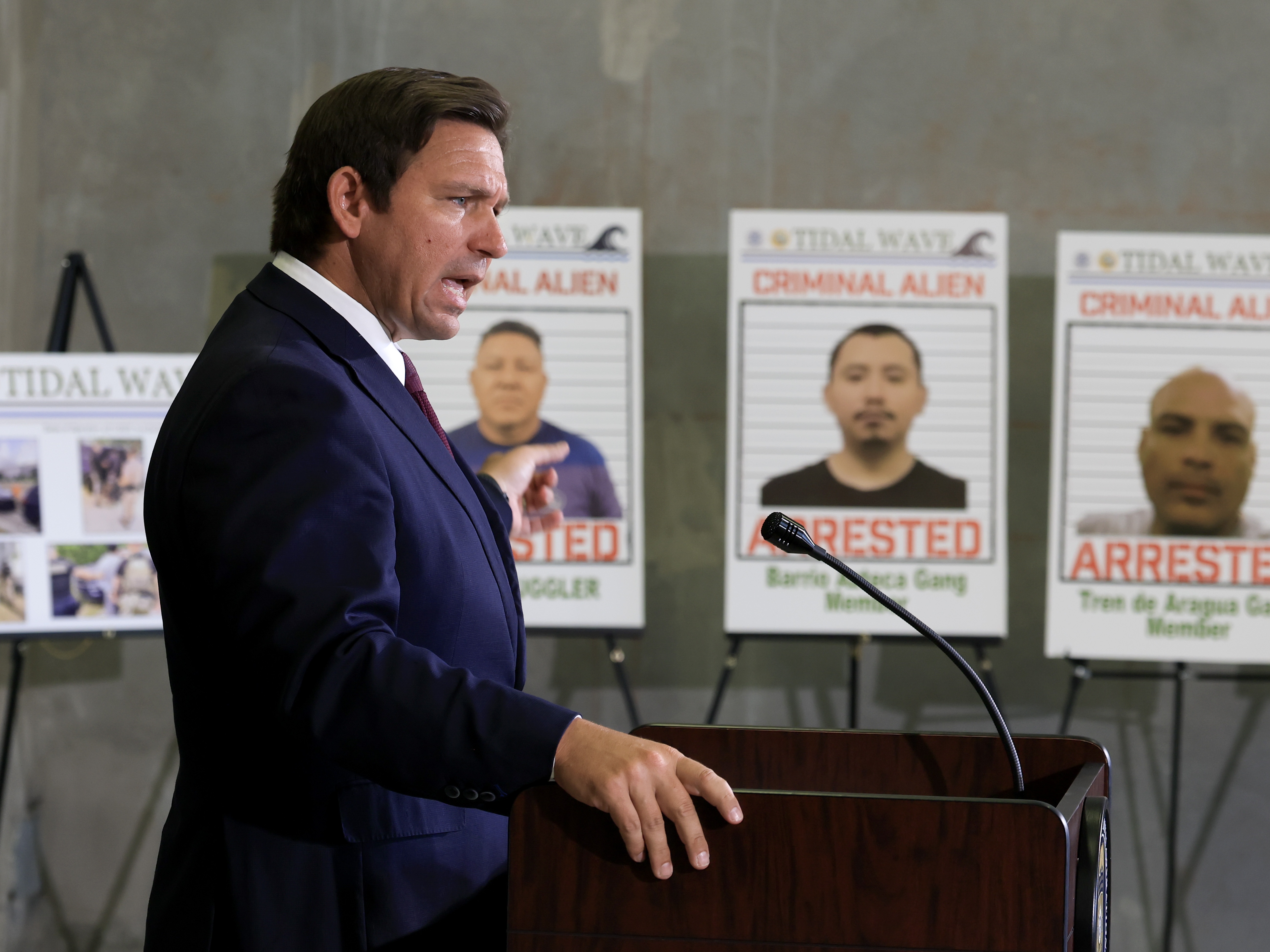 caption: Florida Gov. Ron DeSantis speaks during a press conference, in front of posters of people that law enforcement arrested. DeSantis talked about a multi-agency immigration enforcement effort named Operation Tidal Wave that they say resulted in more than 1,100 arrests in a single week in Florida.