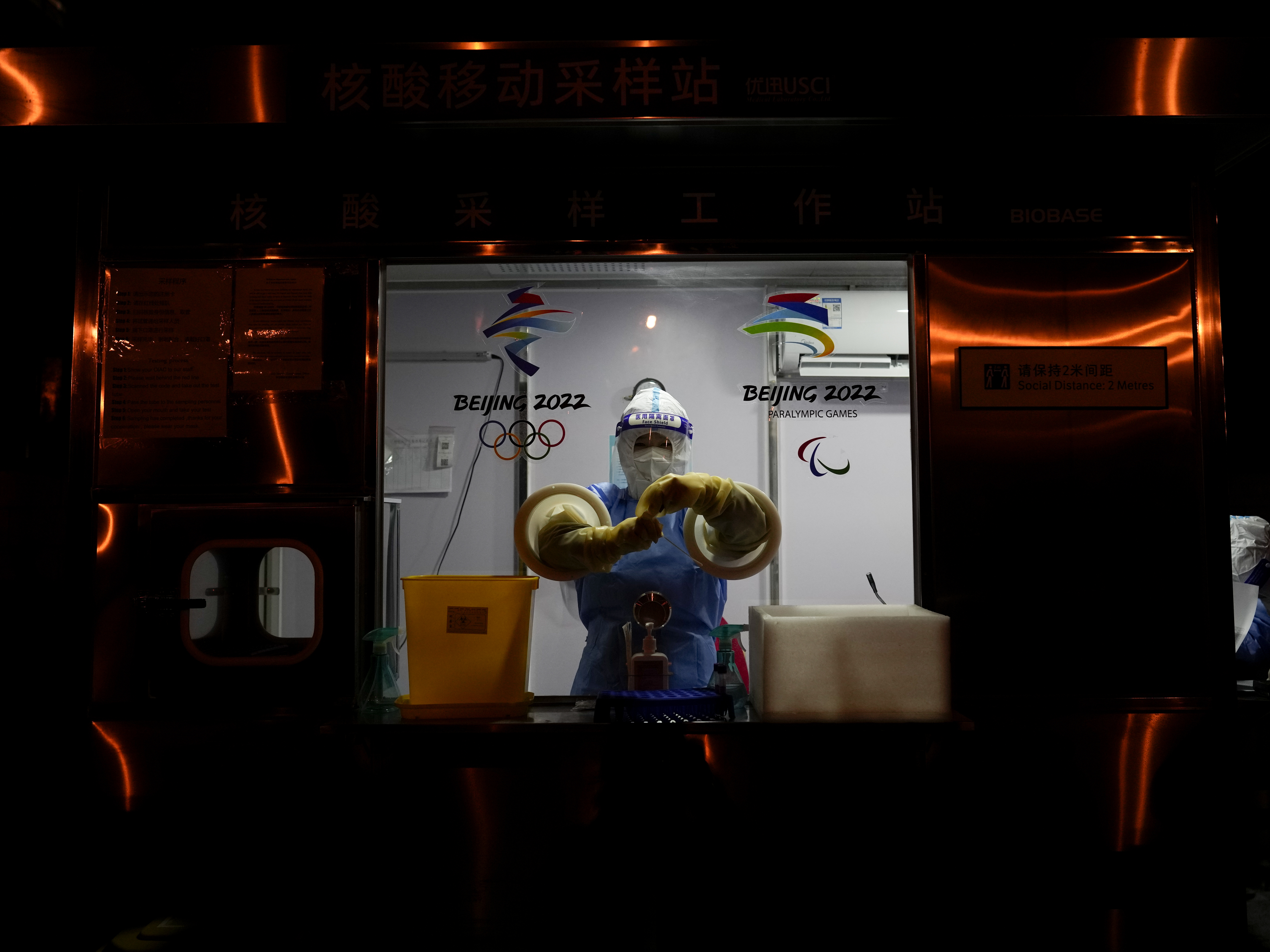 caption: A worker prepares to administer a COVID-19 test at the 2022 Winter Olympics on Wednesday. So far, 111 athletes and officials have tested positive for the virus at the Olympics, including from people arriving at the airport.