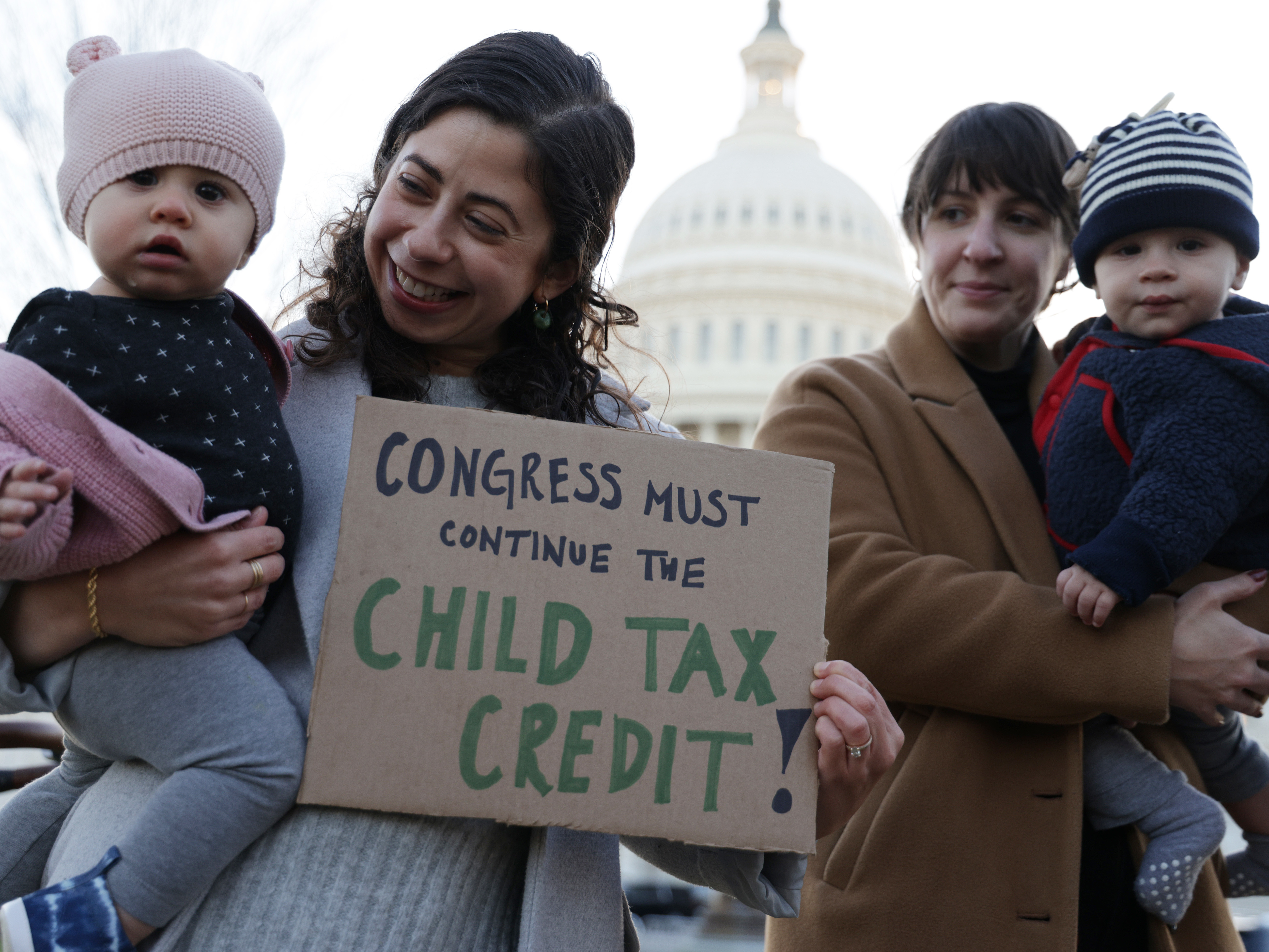 caption: Local residents, Cara Baldari and her nine-month-old daughter Evie (L) and Sarah Orrin-Vipond and her eight-month-old son Otto (R), join a rally in front of the U.S. Capitol December 13, 2021 in Washington, DC. The monthly Child Tax Credit payments expired at the end of last year after Congress failed to renew it.