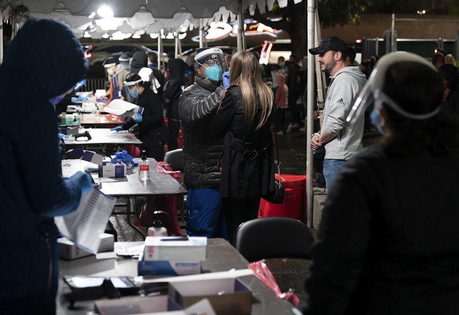 caption: Clinical assistant Richard Wrangel, center left, collects a nasal swab sample from a hockey fan for a COVID-19 test in the parking lot of the Honda Center before an NHL hockey game between the Anaheim Ducks and the Vancouver Canucks, Wednesday, Dec. 29, 2021, in Anaheim, Calif. 