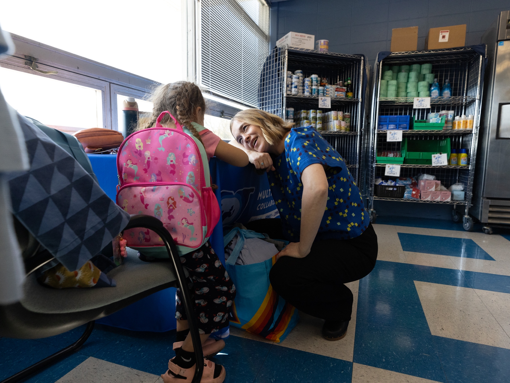 caption: Megan Mainzer, the McKinney-Vento liaison for Middletown Public Schools in Rhode Island, speaks with a young girl at a school food and clothing pantry that's managed, in part, with federal grant money.