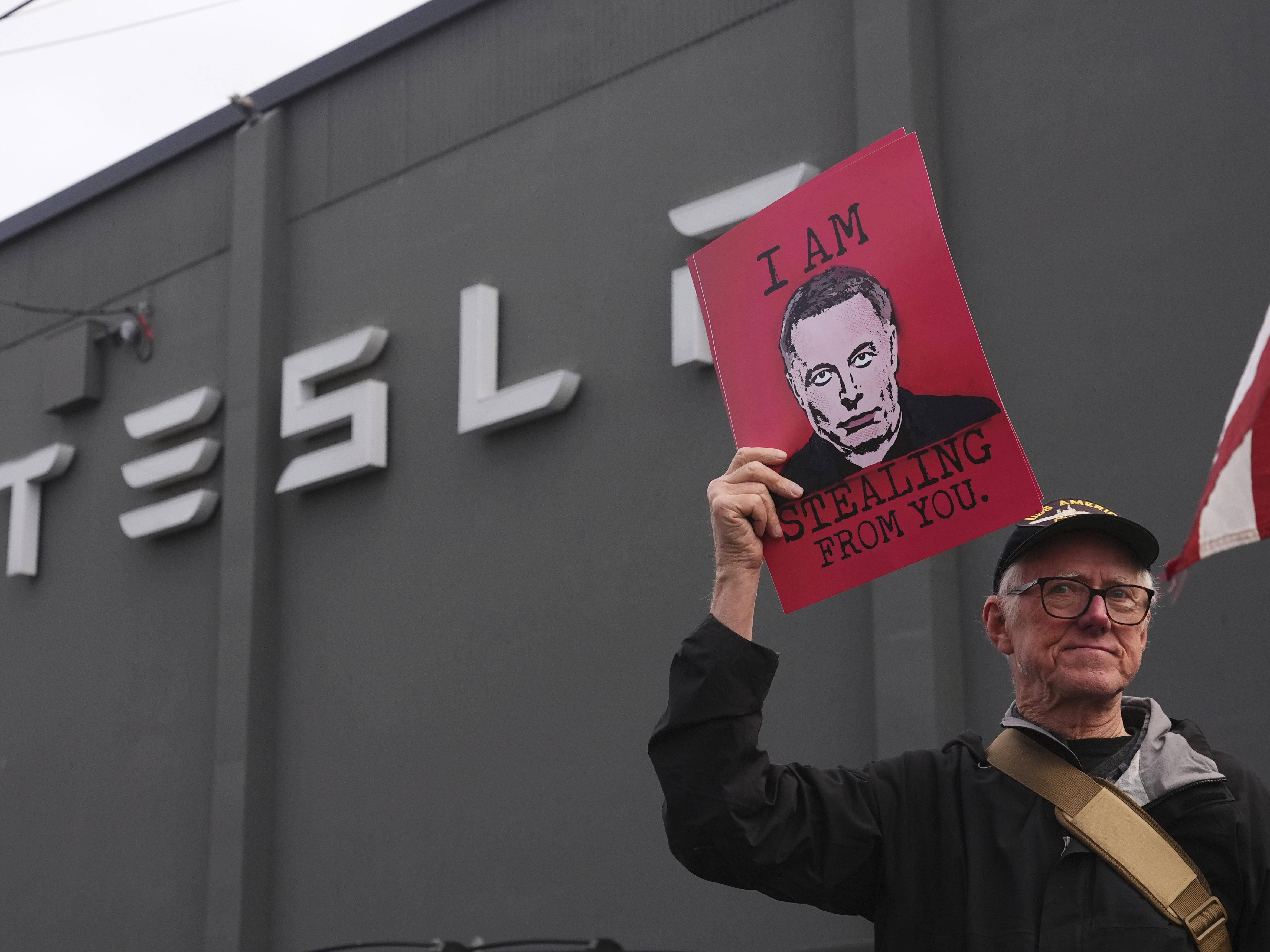 caption: A man holds a sign depicting Elon Musk during a protest against Musk and Tesla on Saturday in Seattle.