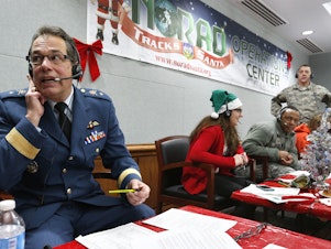 caption: Every year, NORAD staff and volunteers field calls from children inquiring about Santa. Canadian Brig. Gen Guy Hamel joined in the tradition in 2014.