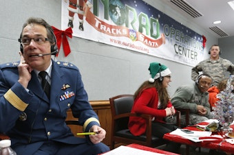 caption: Every year, NORAD staff and volunteers field calls from children inquiring about Santa. Canadian Brig. Gen Guy Hamel joined in the tradition in 2014.