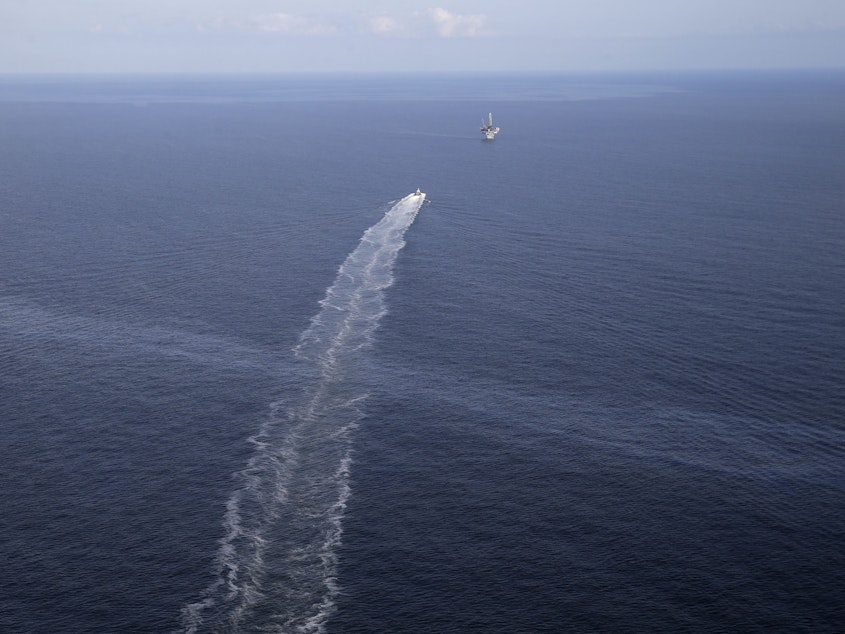 caption: The wake of a supply vessel heading toward a working platform crosses over an oil sheen drifting from the site of the former Taylor Energy oil rig in the Gulf of Mexico in 2015. The Coast Guard says it has contained the oil spill.