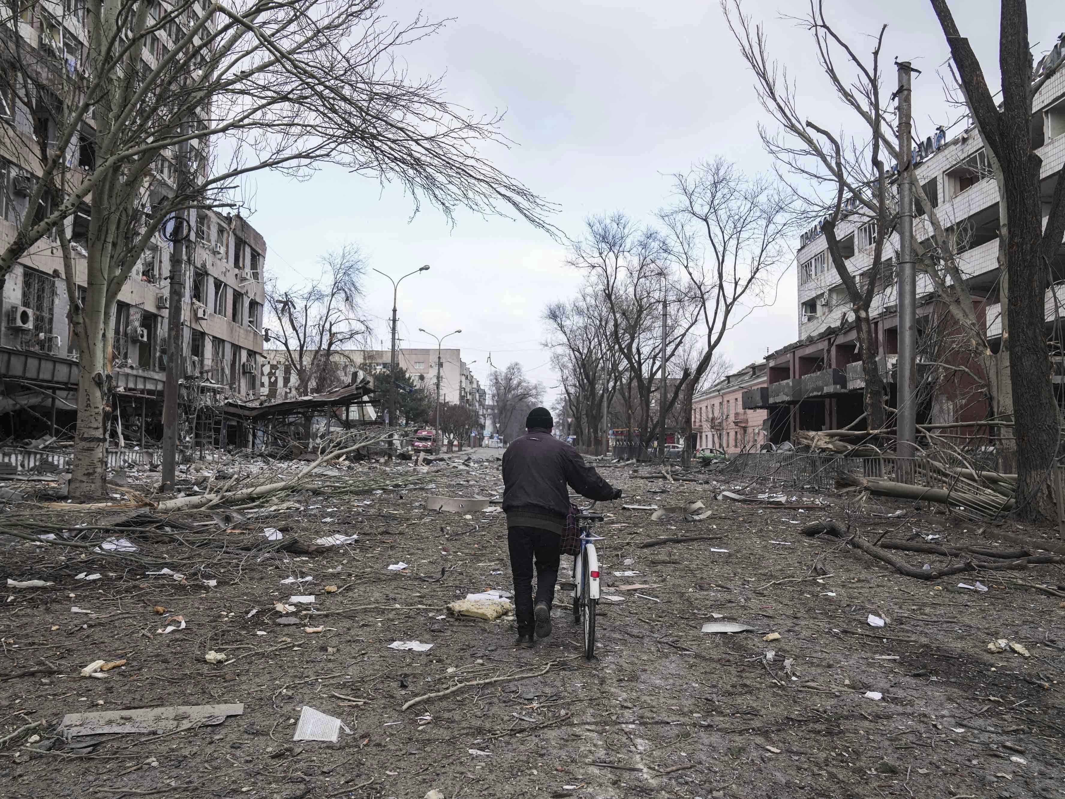 caption: A man walks with a bicycle on a street damaged by shelling in Mariupol, Ukraine, earlier this month.