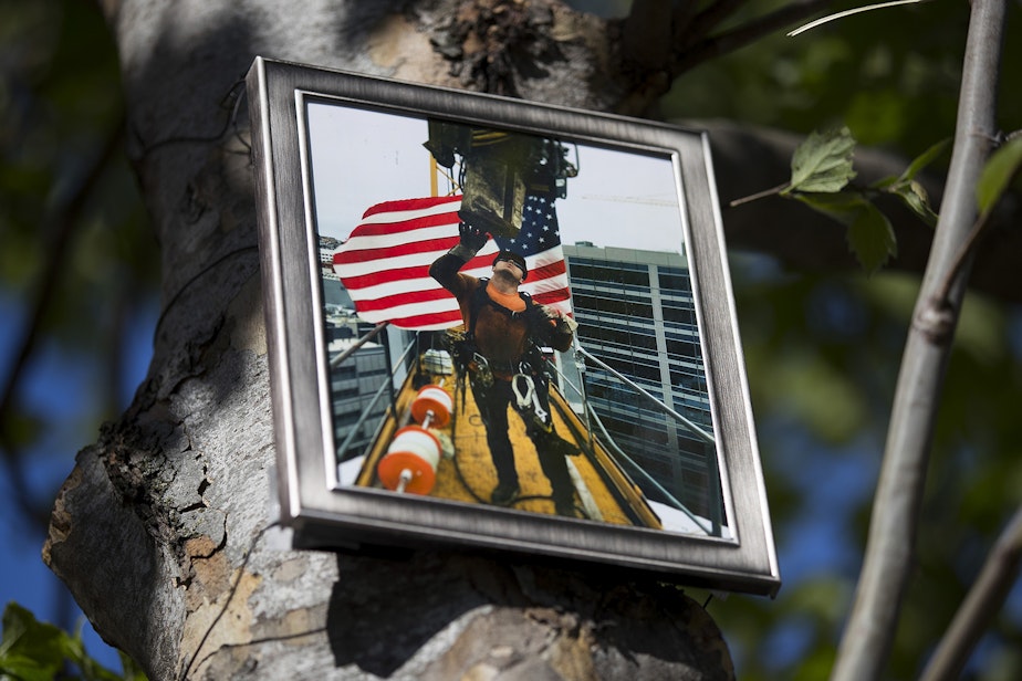 caption: A photograph of ironworker Andrew Yoder is attached to a tree on Monday, April 29, 2019, near a memorial for the victims of the fatal crane collapse along Mercer Street in Seattle.