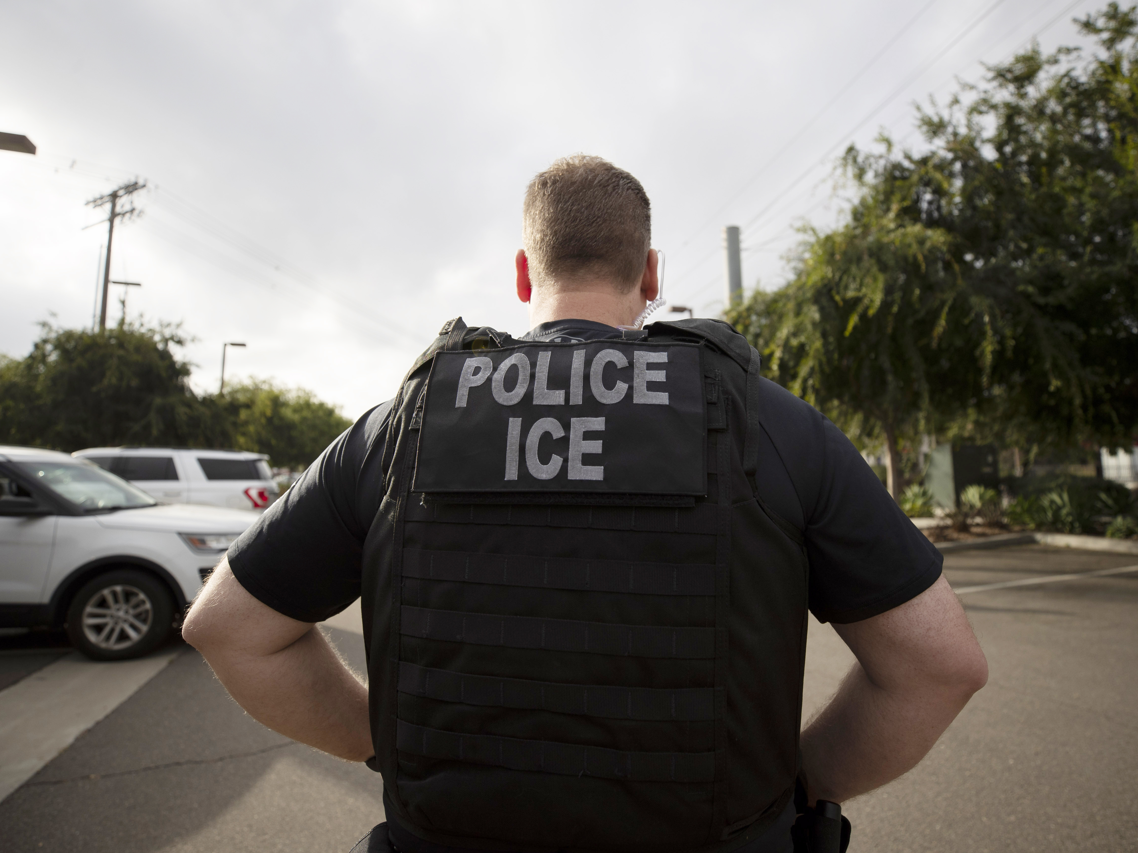 caption: A U.S. Immigration and Customs Enforcement officer looks on during an operation in Escondido, Calif., in 2019. The Biden administration today announced new guidelines that are expected to sharply limit arrests and deportations carried out by ICE.