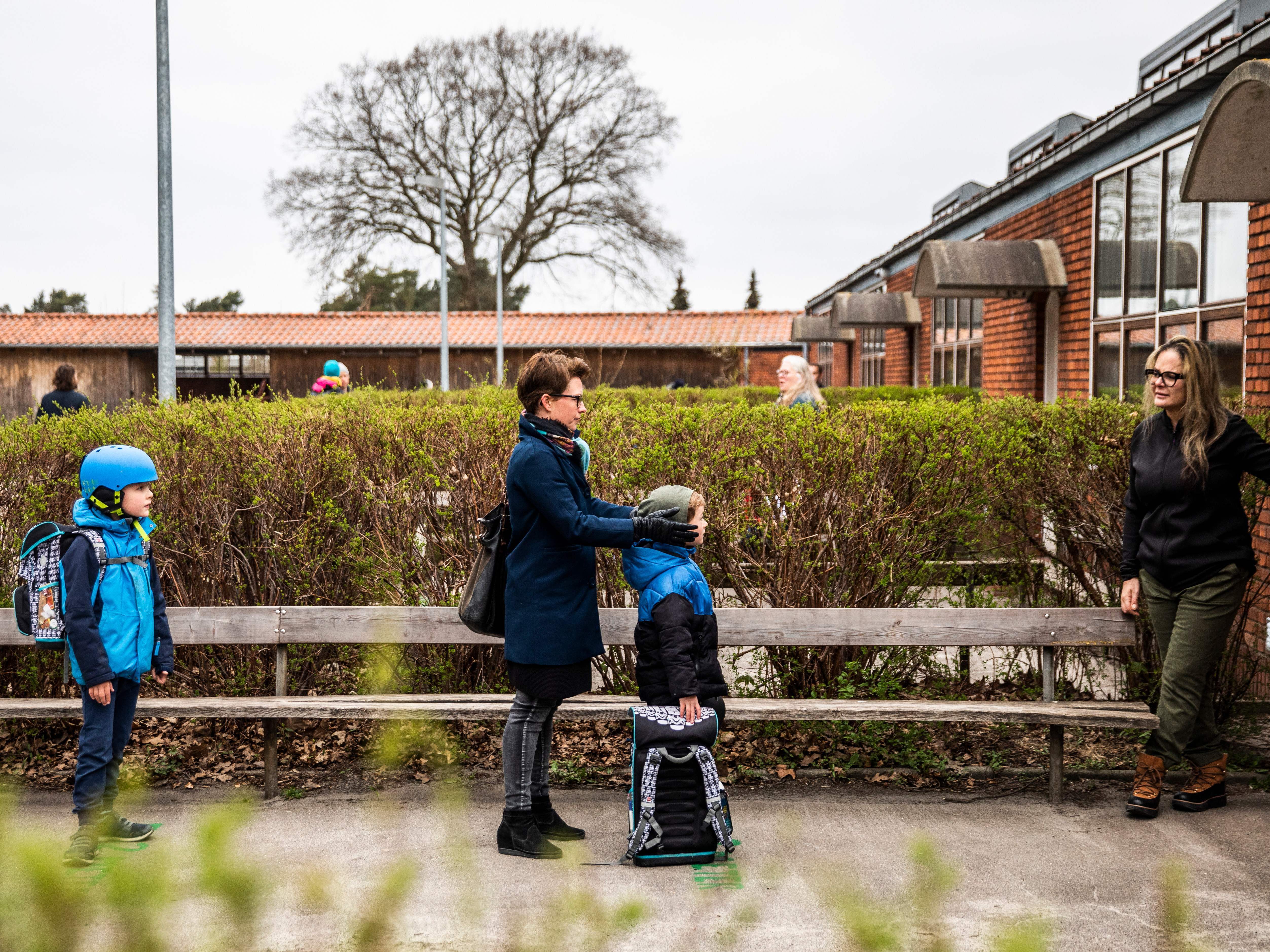 caption: Parents and their children stand in line waiting to get inside Stengaard School north of Copenhagen, Denmark.
