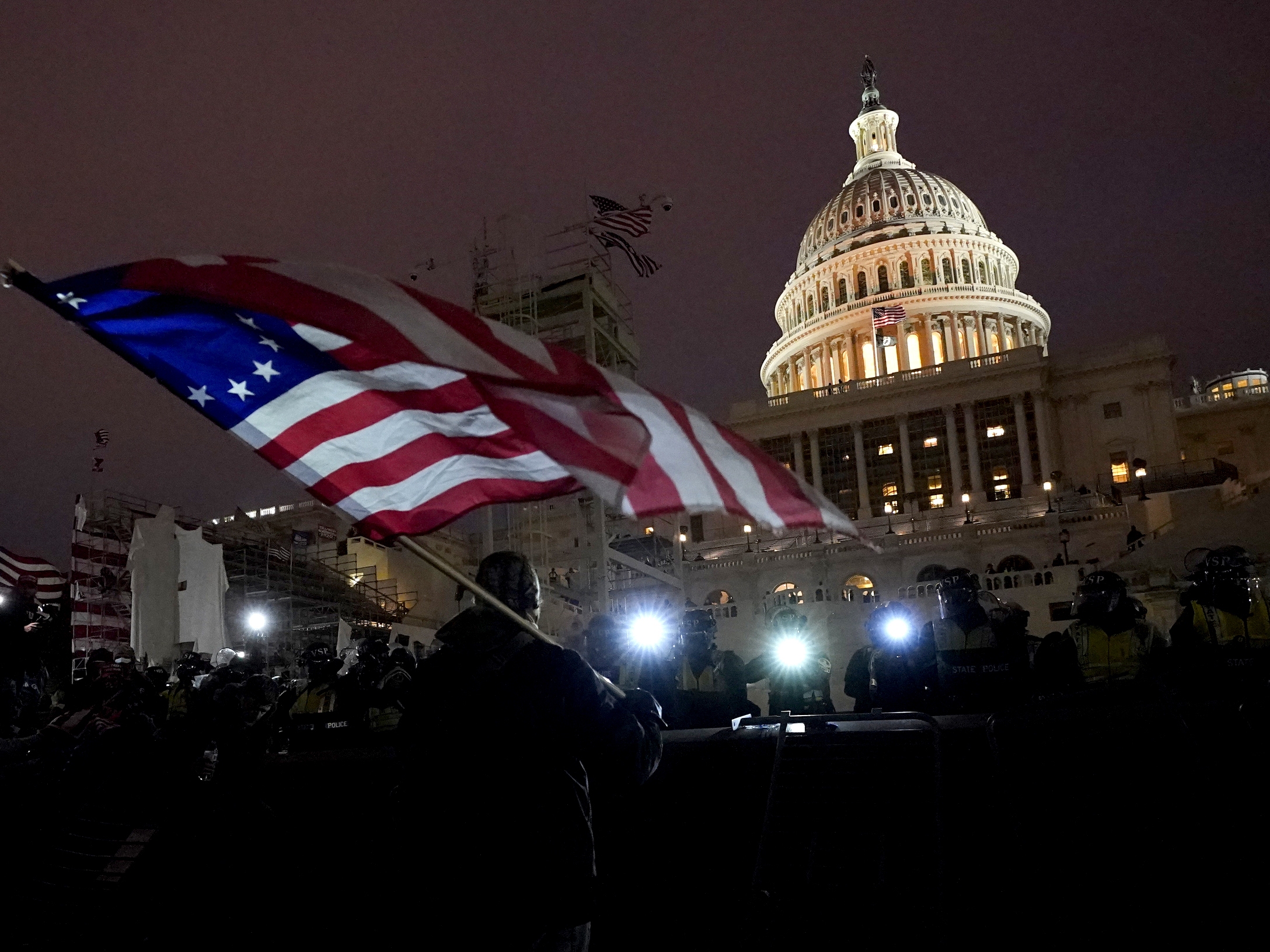 caption: Protesters hold flags as they are pushed back by police on Jan. 6, 2021, after President Trump's supporters stormed the U.S. Capitol. Trump pardoned almost every person who participated in the riot.