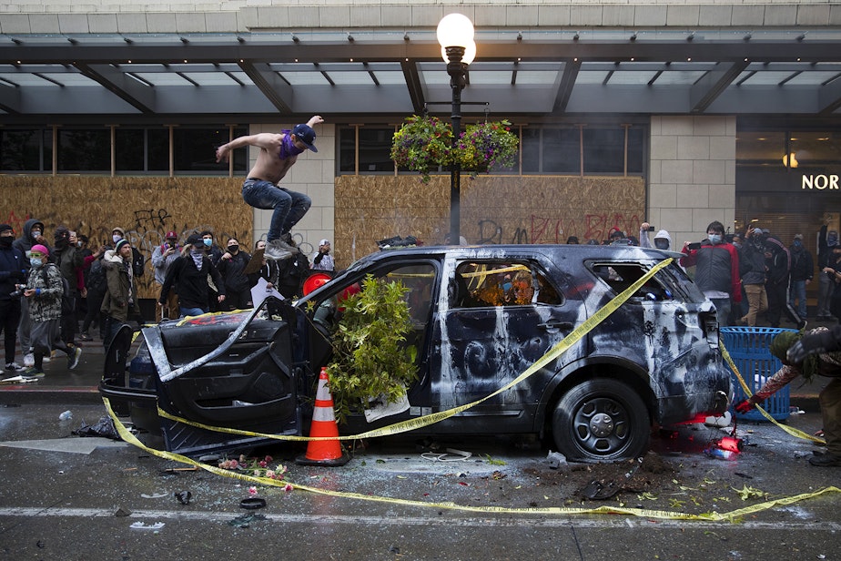 caption: A protester jumps on a Seattle Police car that was later set on fire near the intersection of 5th and Pine Streets on Saturday, May 30, 2020, in Seattle. Thousands gathered in a protest that turned violent following the violent police killing of George Floyd, a black man who was killed by a white police officer who held his knee on Floyd's neck for 8 minutes and 46 seconds, as he repeatedly said, 'I can't breathe,' in Minneapolis on Memorial Day. 