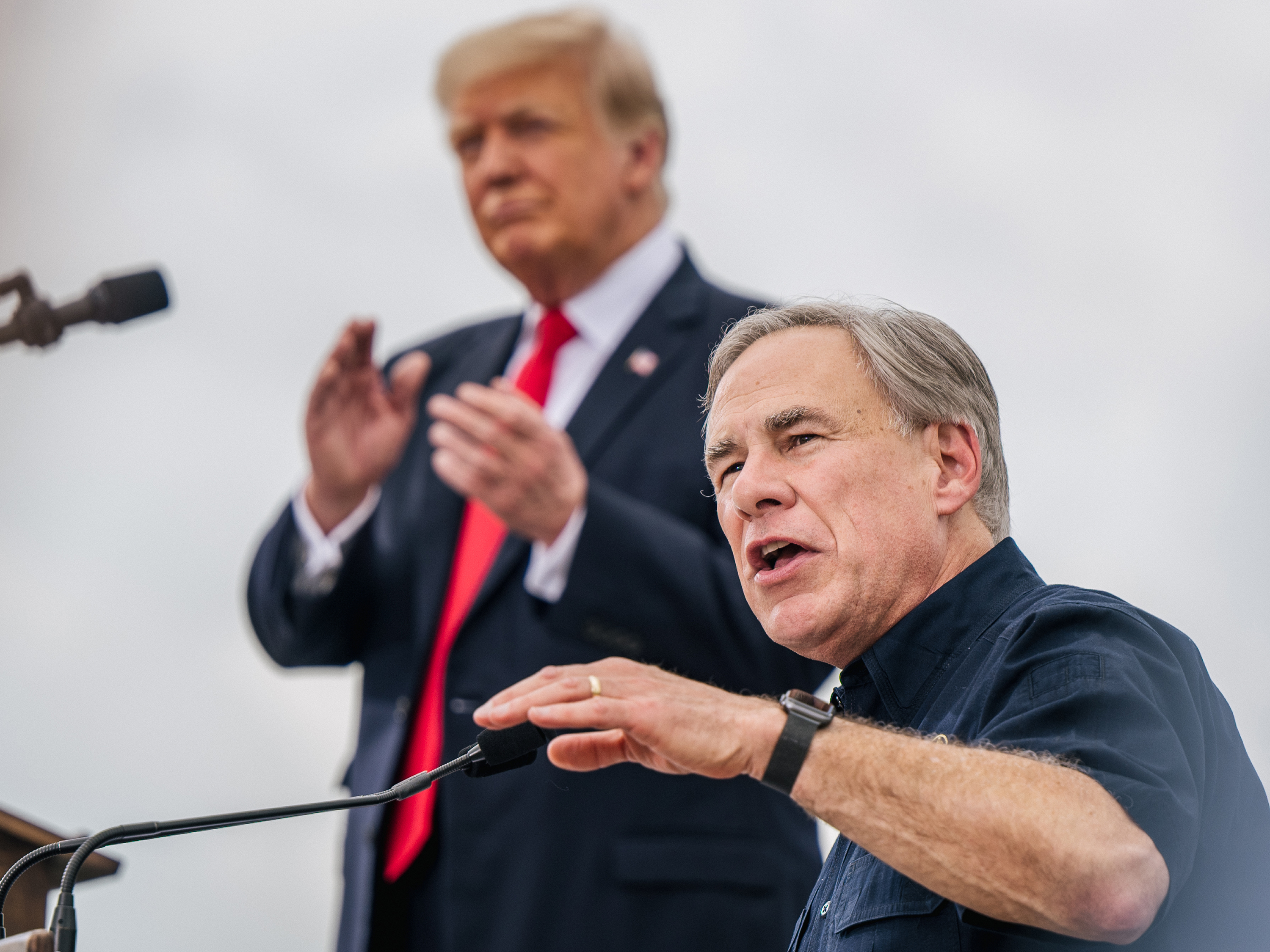 caption: Texas Gov. Greg Abbott speaks alongside former President Donald Trump during a tour of an unfinished section of the border wall on June 30 in Pharr, Texas. Abbott says he'll continue Trump's border barrier, a pledge that is expected to help the governor in his reelection campaign.