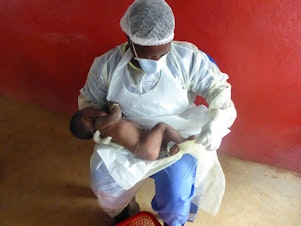 caption: A health care worker gives some much needed maternal care to an infant whose mother died from Ebola.