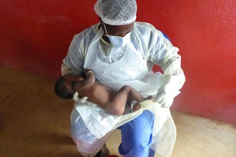caption: A health care worker gives some much needed maternal care to an infant whose mother died from Ebola.