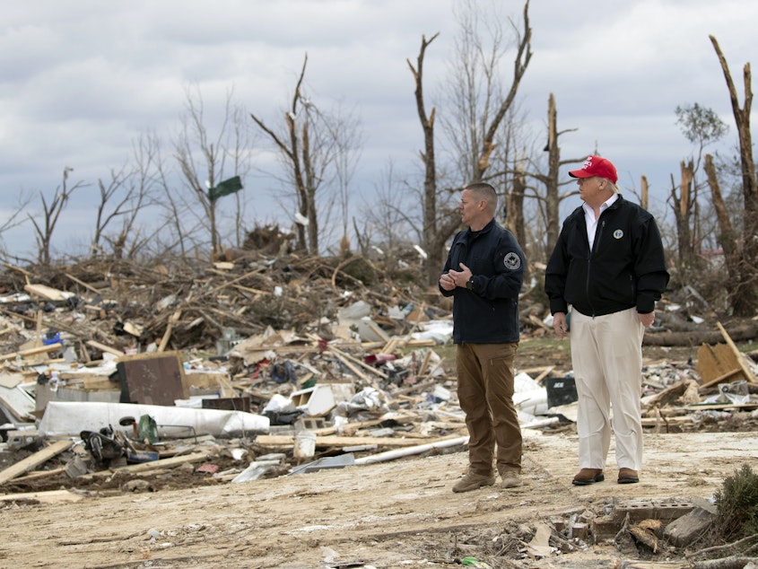 caption: President Donald Trump speaks with a Putnam County rescue worker as he tours the damage left by the tornadoes in Cookeville, Tenn.