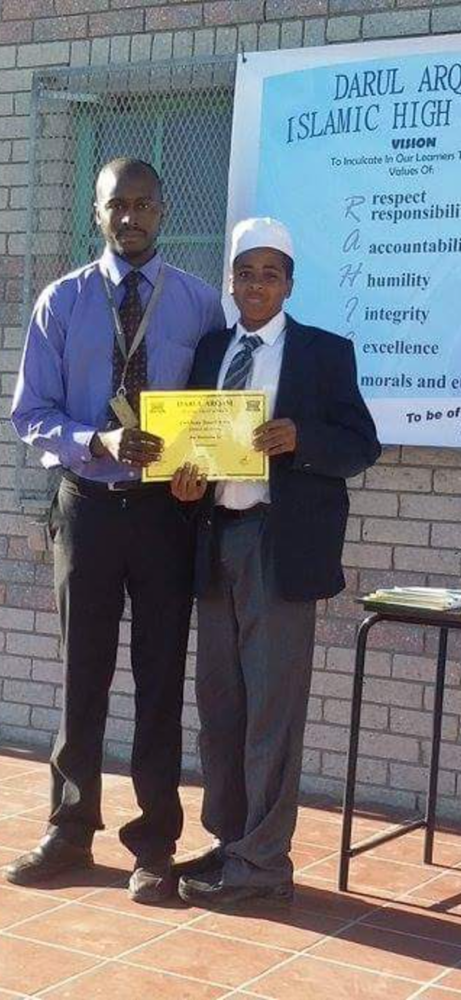 caption: Ahmed Ahmed (right) poses with his father at his 8th grade award ceremony in 2015 in Darul Arqam Islamic High School  in Cape Town, South Africa.