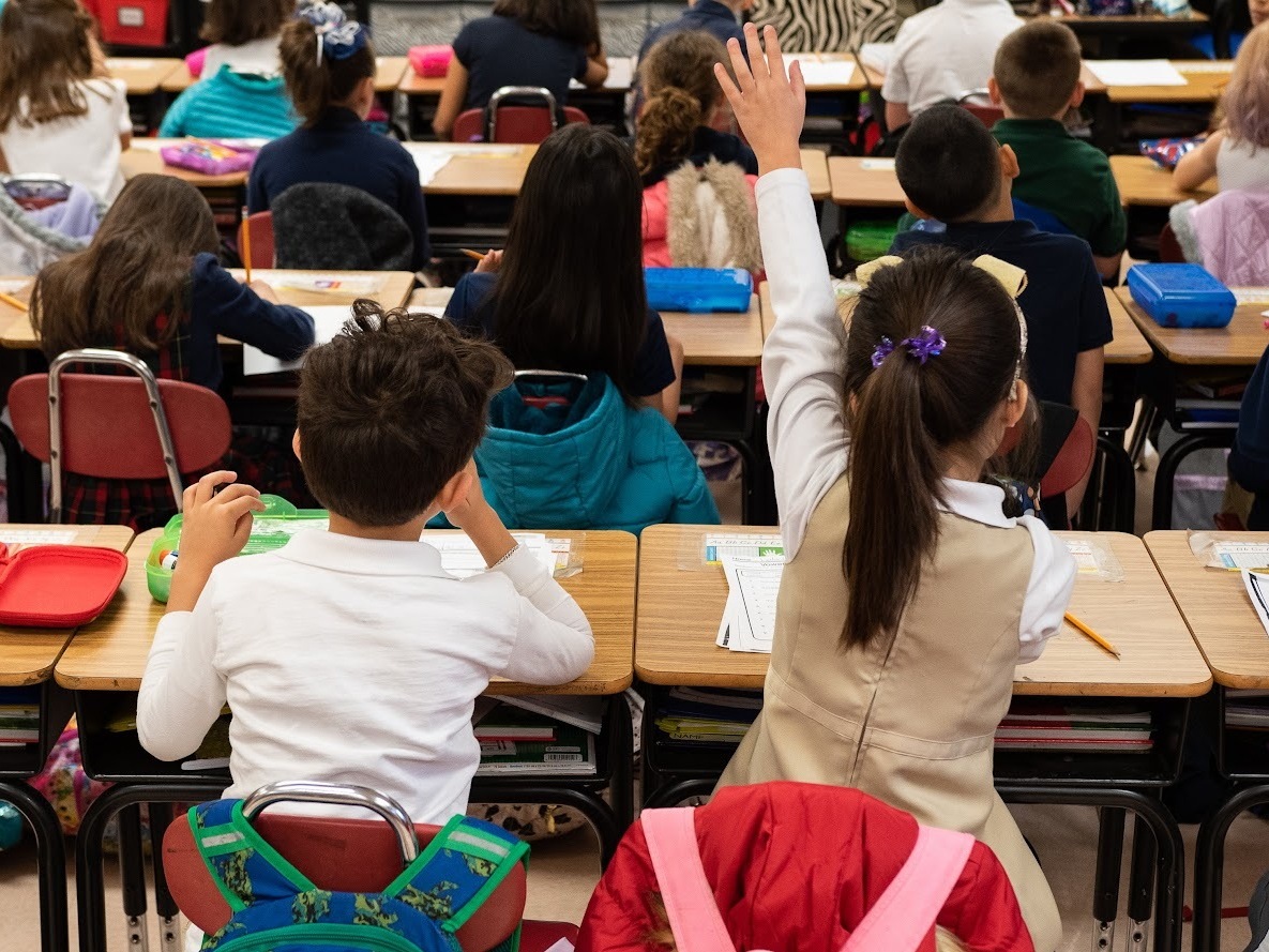 caption: A second grader raises her hand in class at Nichols Hills Elementary School in Oklahoma City in 2020. Under a new bonus program aimed at addressing teacher shortages, over 500 educators received bonuses of up to $50,000.