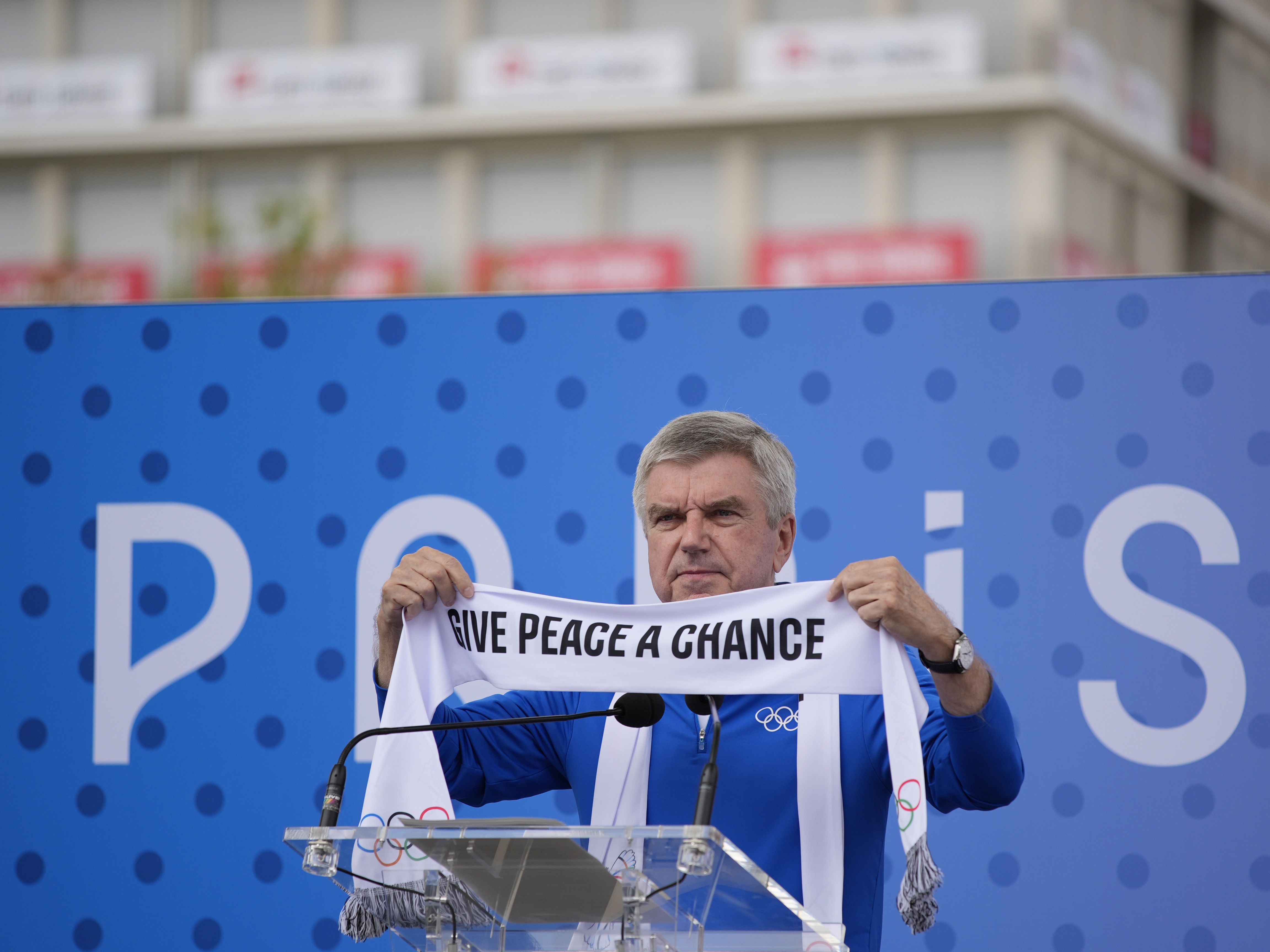 caption: IOC President Thomas Bach holds a scarf during the inauguration of the Olympic Truce Wall in the Olympic Village at the 2024 Summer Olympics on Monday in Paris, France.