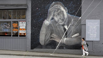 caption: A woman walks past a large mural of the Rev. Martin Luther King Jr. on the side of a diner, painted by artist James Crespinel in the 1990's and later restored, along Martin Luther King Jr. Way, Tuesday, April 3, 2018, in Seattle.