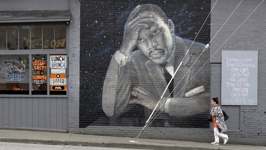 caption: A woman walks past a large mural of the Rev. Martin Luther King Jr. on the side of a diner, painted by artist James Crespinel in the 1990's and later restored, along Martin Luther King Jr. Way, Tuesday, April 3, 2018, in Seattle.