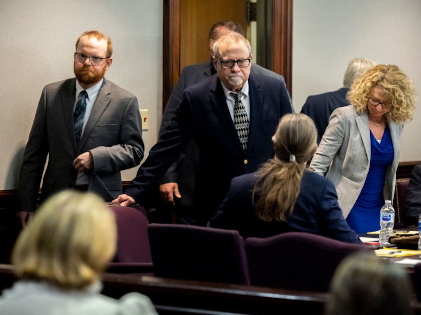 caption: Greg McMichael (center) and his son Travis McMichael (left) look at family members seated in the gallery when they walk into the courtroom for the reading of the jury's verdict for themselves and a neighbor, William "Roddie" Bryan, in the Glynn County Courthouse on Nov. 24, 2021, in Brunswick, Ga. The three men were charged with the fatal shooting of 25-year-old Ahmaud Arbery in 2020.