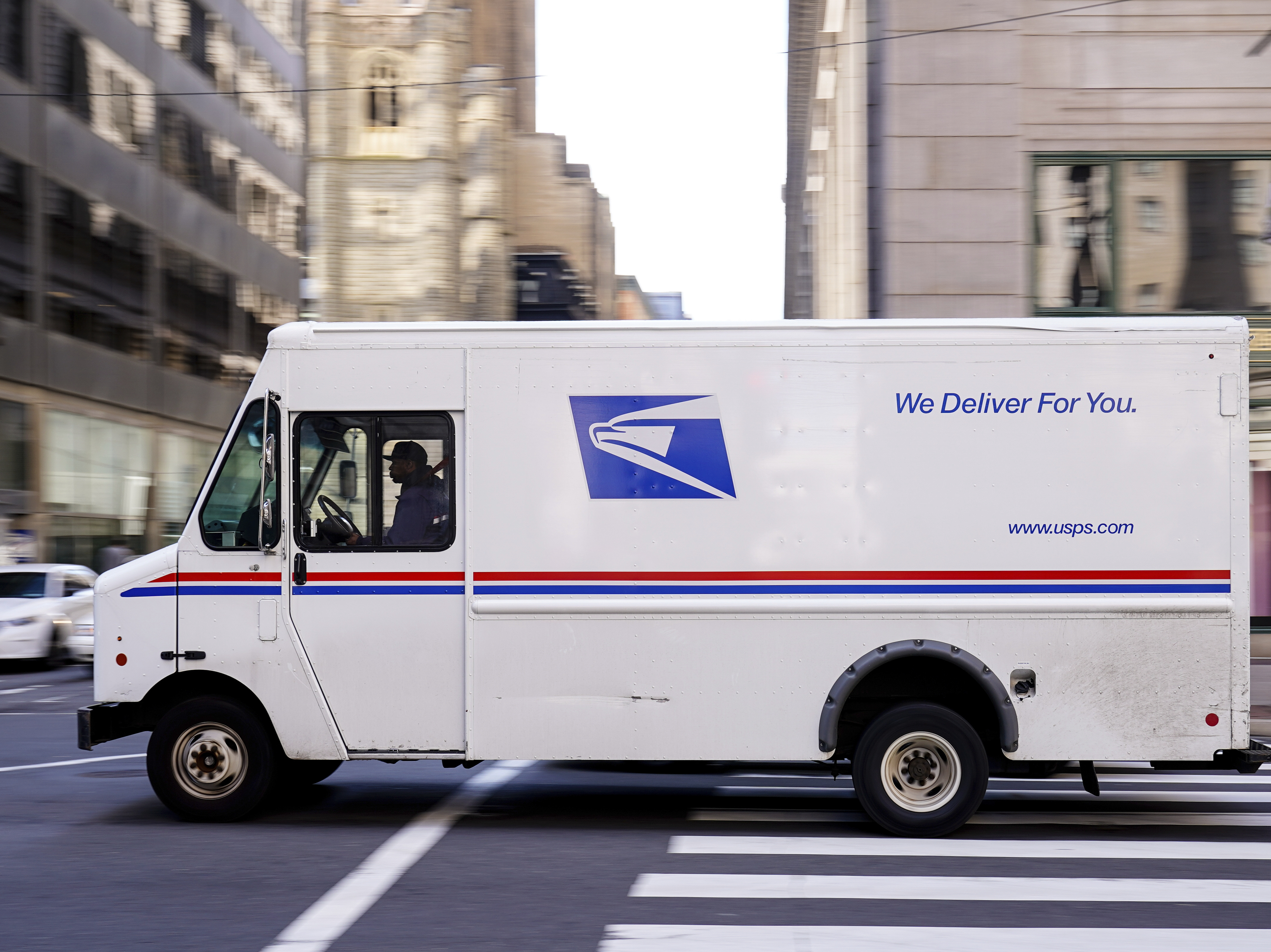caption: A U.S. Postal Service truck drives in Philadelphia. The service is about to set longer delivery standards for first-class packages, in a move that its regulator says will not have a big effect on its finances.