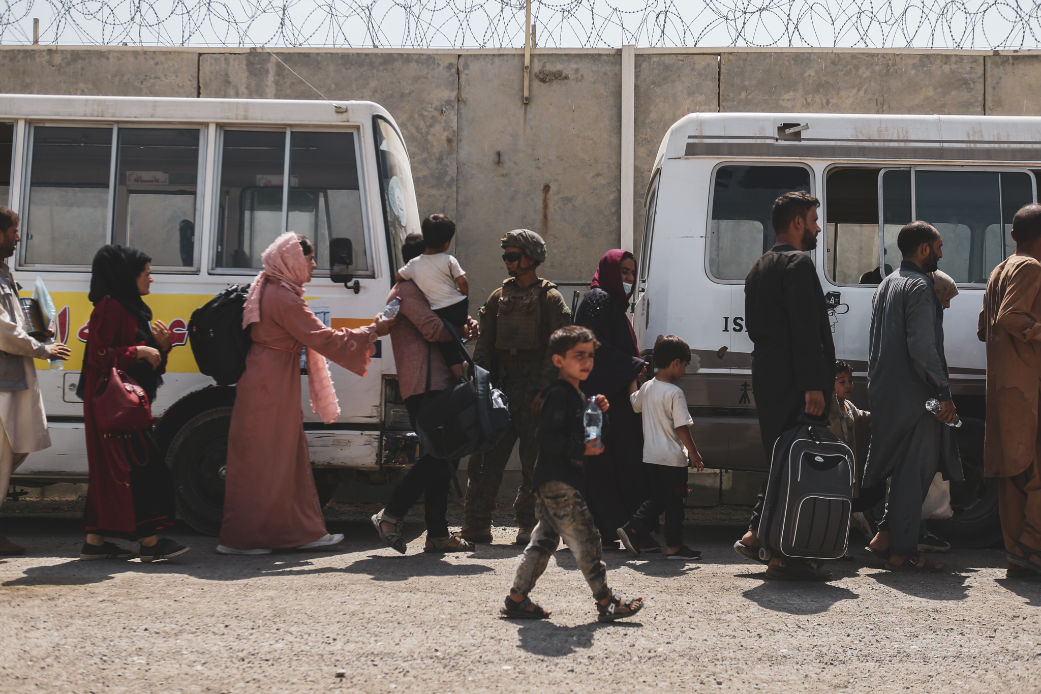 caption: KABUL, AFGHANISTAN - AUGUST 21:  In this handout provided by the U.S. Marine Corps, evacuees board buses for processing at Hamid Karzai International Airport during the evacuation on August 21, 2021 in Kabul, Afghanistan. The U.S. military is assisting in the evacuation effort.  (Photo by Isaiah Campbell/U.S. Marine Corps via Getty Images)