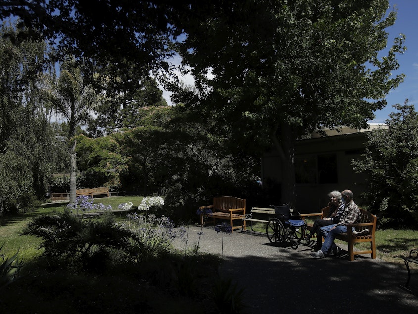 caption: Larry Yarbroff visits his wife Mary at Chaparral House in Berkeley, Calif. in July. California health authorities had allowed some visits to resume, and now federal regulators are doing the same, with measures to try to block the spread of the coronavirus.