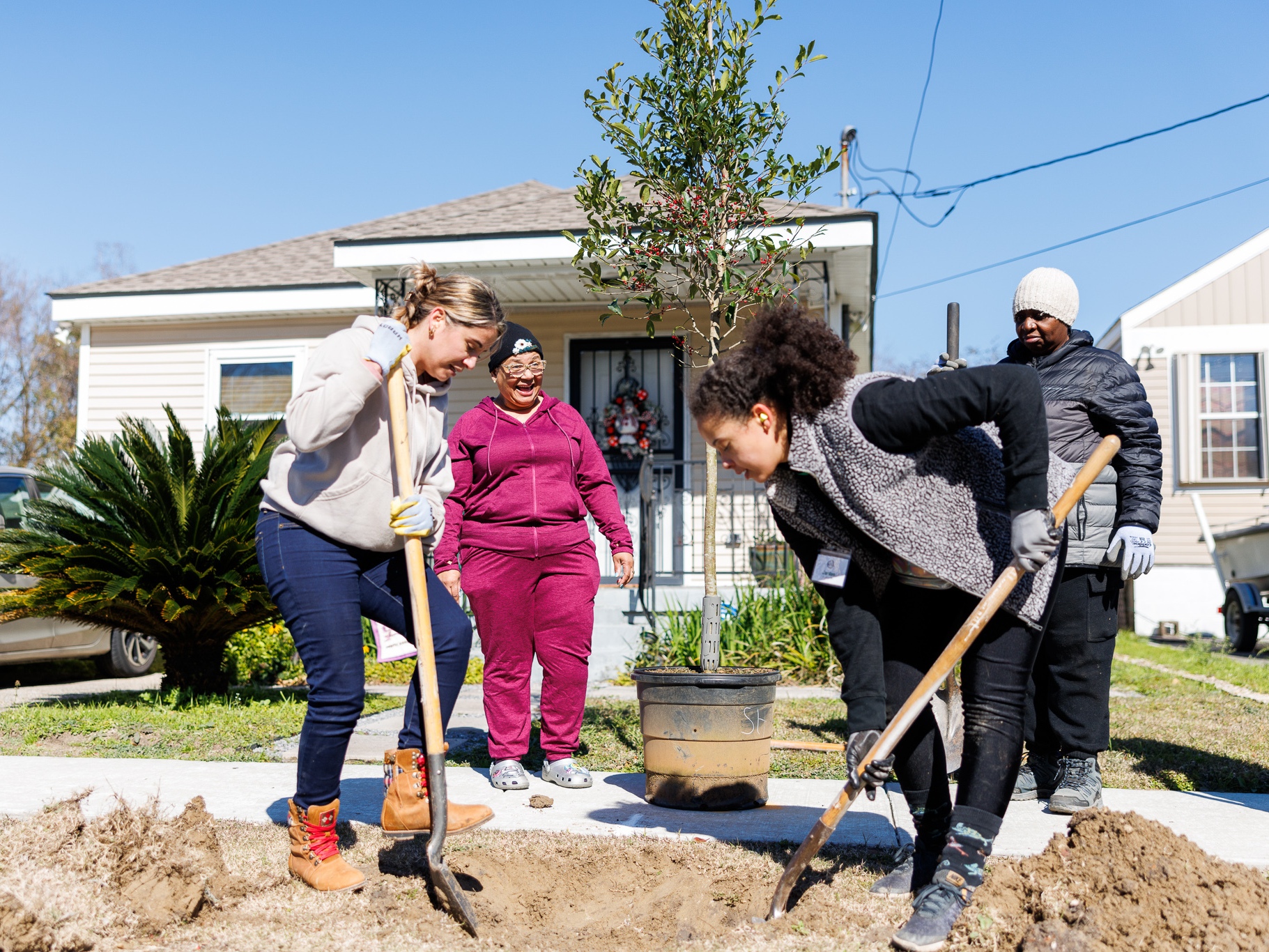 caption: Volunteers Olly De Almeida (left), Jordan Bordenave (right) and Rosemary White (far right) plant a tree in front of Tribble Condor's (center) house in New Orleans' Lower 9th Ward. The project was funded by a federal grant terminated in February.