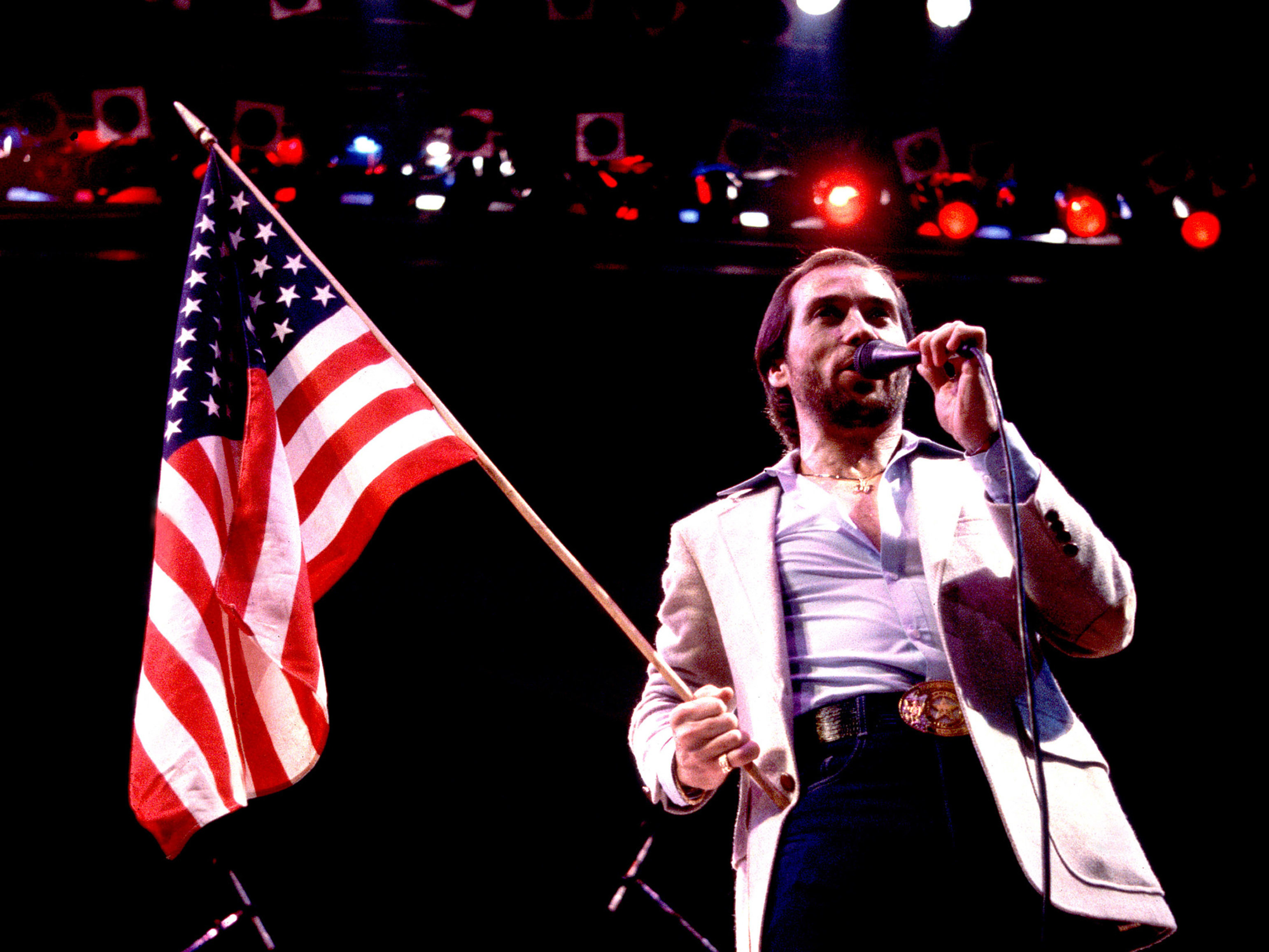 caption: Lee Greenwood performs in Illinois in 1984. Released that spring to a modest chart showing, "God Bless the U.S.A." found staying power as political campaigns began to adopt it.