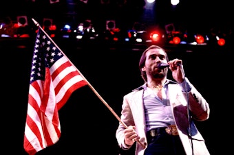 caption: Lee Greenwood performs in Illinois in 1984. Released that spring to a modest chart showing, "God Bless the U.S.A." found staying power as political campaigns began to adopt it.