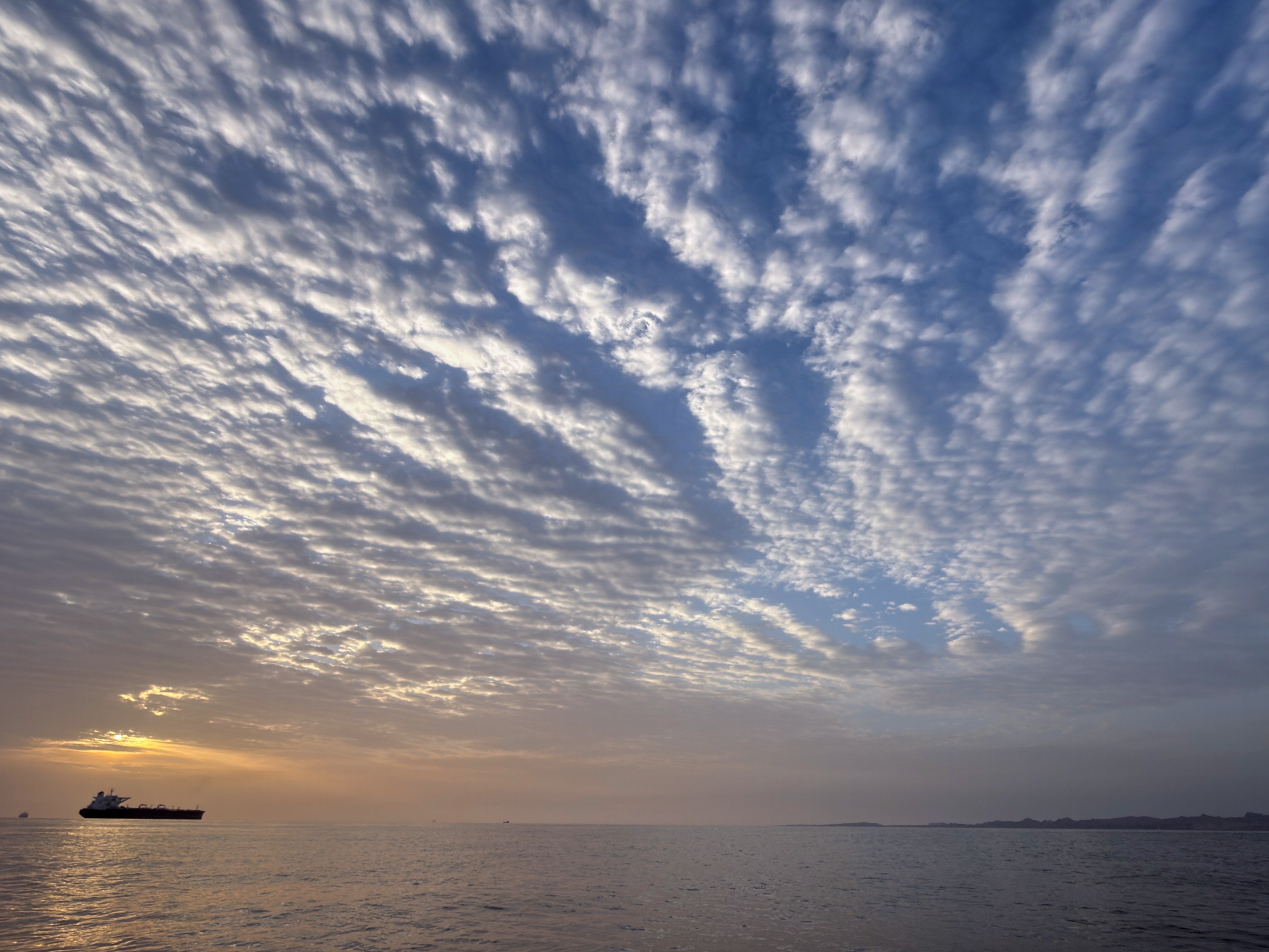caption: The sun rises behind a tanker anchored in the Strait of Hormuz off the coast of Qeshm Island, Iran, Saturday, April 18, 2026.