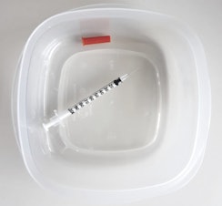 caption: A needle from the needle exchange off University Way ... in a Rubbermaid plastic container (not a Tupperware).