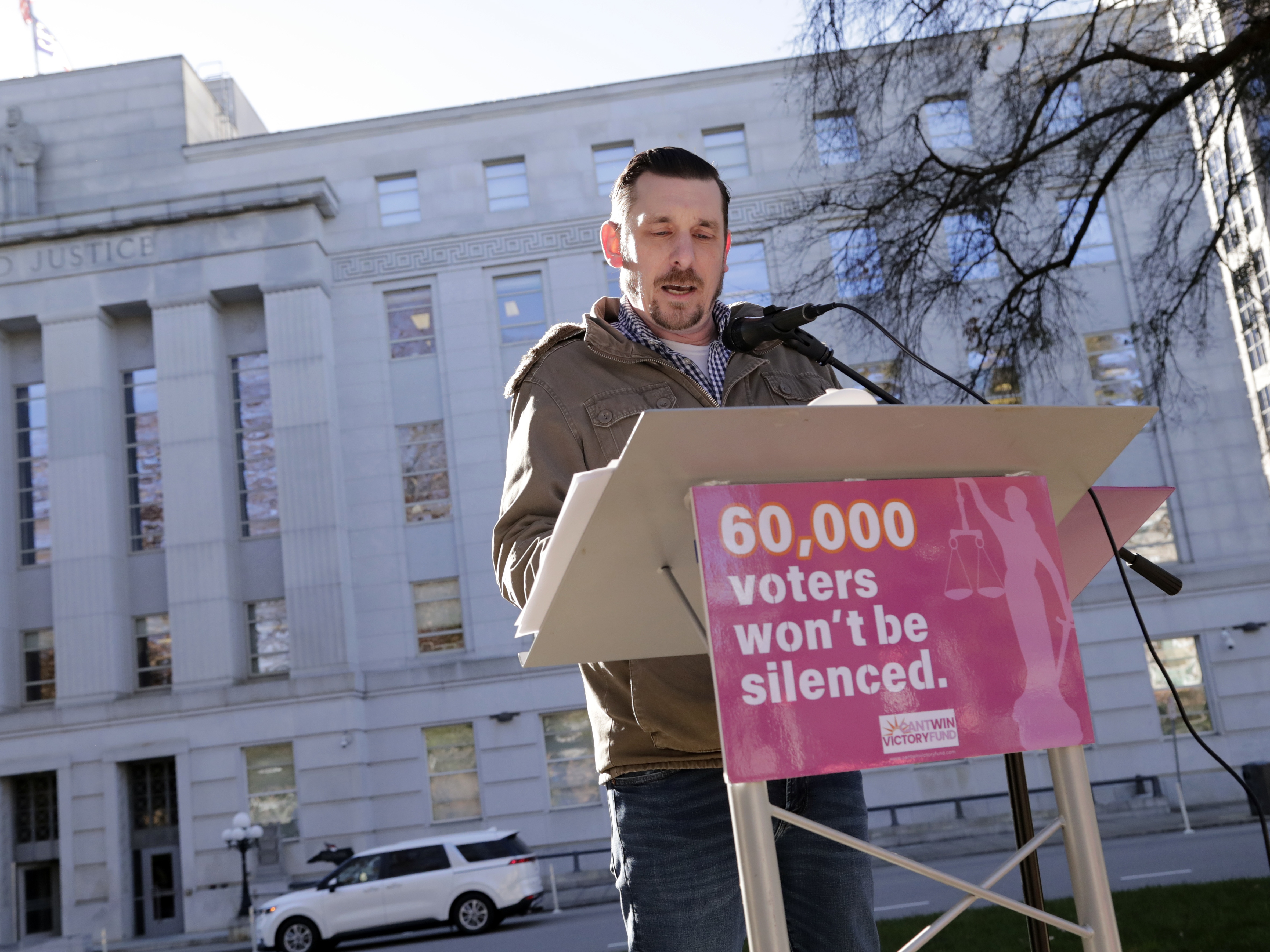 caption: Standing in front of the North Carolina Supreme Court in Raleigh on Jan. 14, Ted Corcoran reads a list of over 60,000 people who cast ballots in the November 2024 election but whose votes have been challenged by Republican court candidate Jefferson Griffin in his extremely close race with Democratic Justice Allison Riggs.