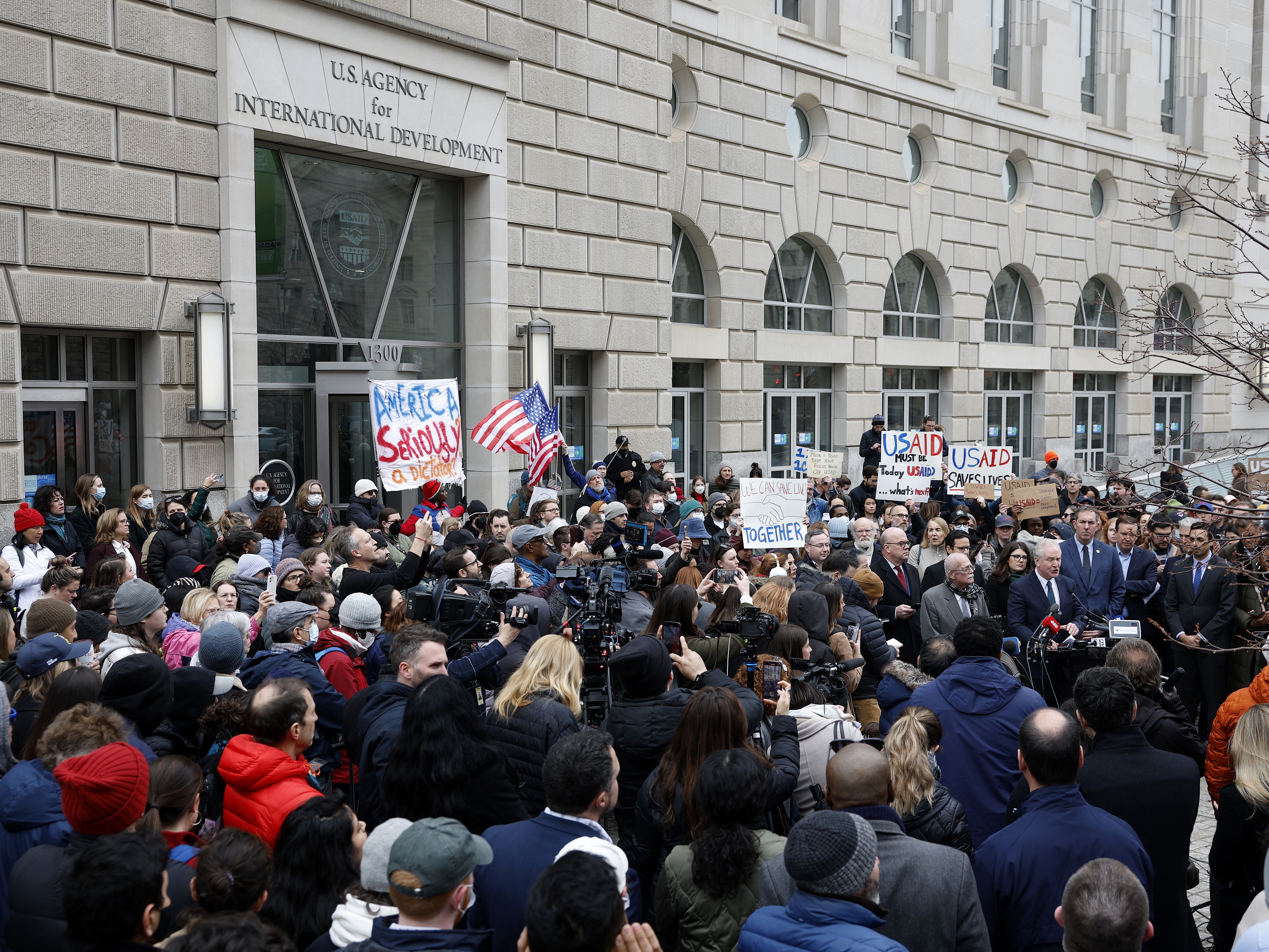 caption: The Trump administration's plans for mass firings are sparking protests and challenges in court. Here, supporters of the U.S. Agency for International Development join Sen. Chris Van Hollen, D-Md., and Rep. Gerry Connolly, D-Va., outside USAID's headquarters in Washington, D.C., on Feb. 3 after Elon Musk, who oversees the Department of Government Efficiency, said he and President Trump would close the foreign assistance agency.