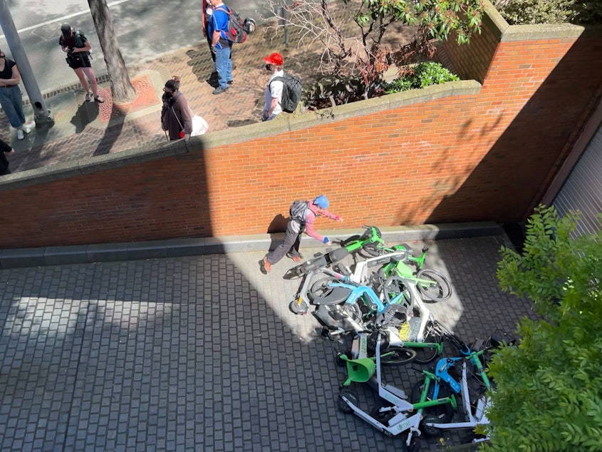 caption: A protester drops an e-bike in front of the Madison Street exit from the Henry M. Jackson Federal Building in Seattle on June 10, 2025.