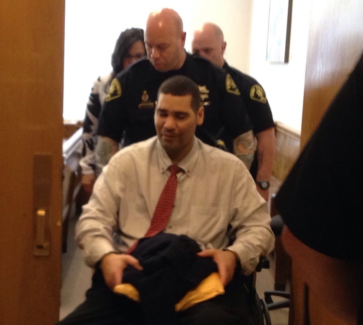 caption: Guards wheel Monfort from the courtroom on Wednesday. Monfort is paralyzed from the waist down.