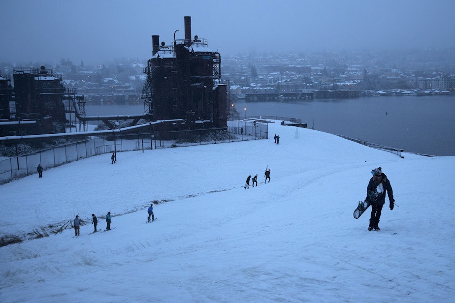 caption: Alec Pflaster, right, carries his snowboard to the top of the hill on Monday, February 11, 2019, at Gas Works Park in Seattle.