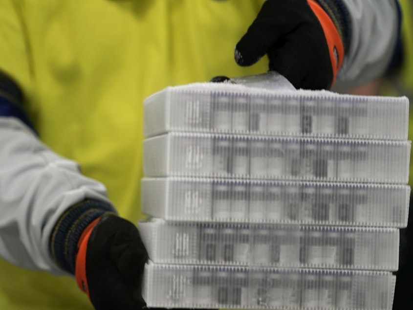 caption: A worker carries boxes containing the Pfizer-BioNTech COVID-19 vaccine that were being prepared for shipment from a Pfizer facility in Portage, Mich., in December.