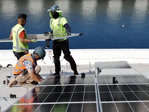 caption: Workers install solar panels at the Port of Los Angeles in California.
