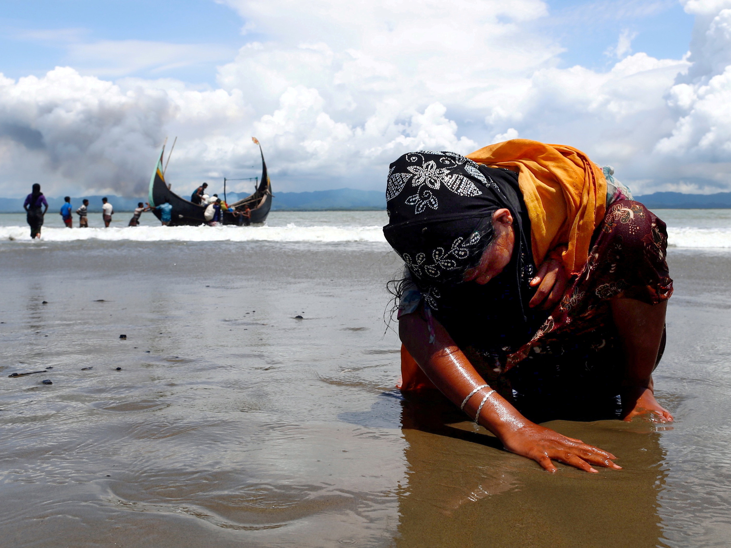 caption: An exhausted Rohingya refugee woman touches the shore after crossing the Bangladesh-Myanmar border by boat through the Bay of Bengal, in Shah Porir Dwip, Bangladesh, on Sept. 11, 2017.