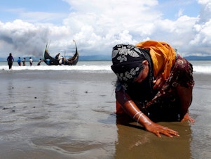 caption: An exhausted Rohingya refugee woman touches the shore after crossing the Bangladesh-Myanmar border by boat through the Bay of Bengal, in Shah Porir Dwip, Bangladesh, on Sept. 11, 2017.