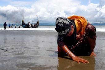 caption: An exhausted Rohingya refugee woman touches the shore after crossing the Bangladesh-Myanmar border by boat through the Bay of Bengal, in Shah Porir Dwip, Bangladesh, on Sept. 11, 2017.