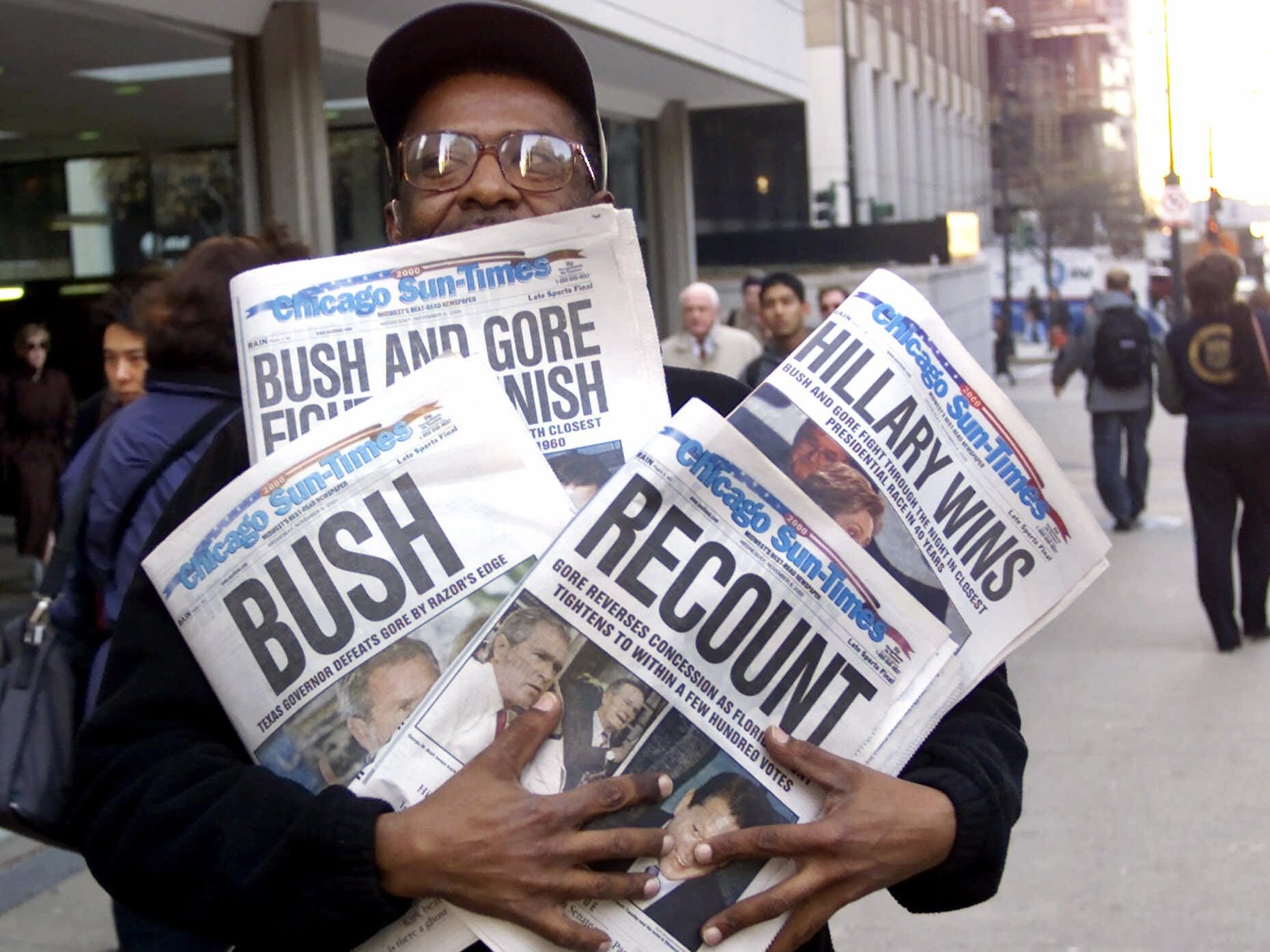 caption: A man holds four copies of the Chicago Sun-Times, each with a different headline, on Nov. 8, 2000.