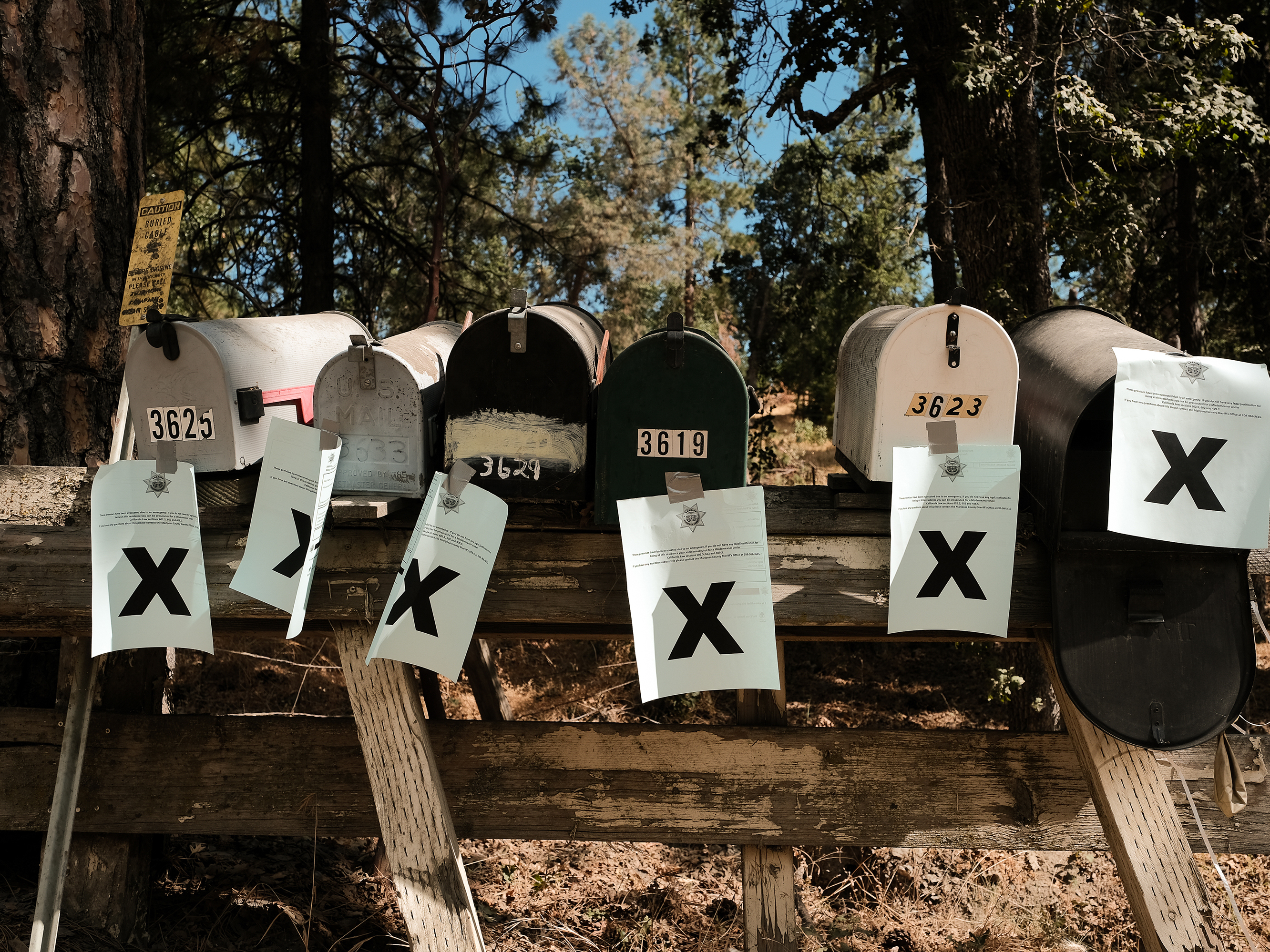 caption: A row of mailboxes tagged with evacuation notices during the Oak Fire in Mariposa, Calif., in July 2022. Many residents in the area are losing their home insurance because of rising wildfire risk.
