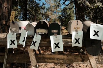 caption: A row of mailboxes tagged with evacuation notices during the Oak Fire in Mariposa, Calif., in July 2022. Many residents in the area are losing their home insurance because of rising wildfire risk.